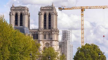 Die beiden Kirchtürme der Notre Dame. Rechts im Bild steht ein großer, gelber Baukran. Es ist bewölkt und die Bäume sind grün.