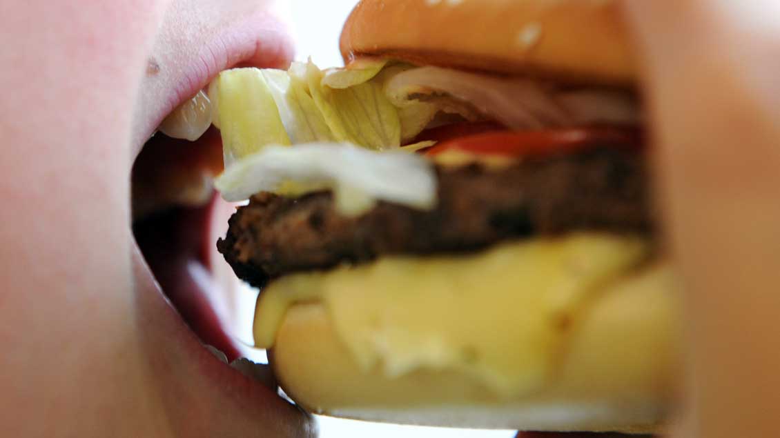 Ein Mensch beißt genüsslich in einen Hamburger. Foto: Michael Bönte