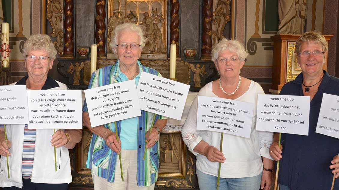 Vier Frauen zeigen auf kleinen Schildern Forderungen nach Gleichberechtigung in der Kirche
