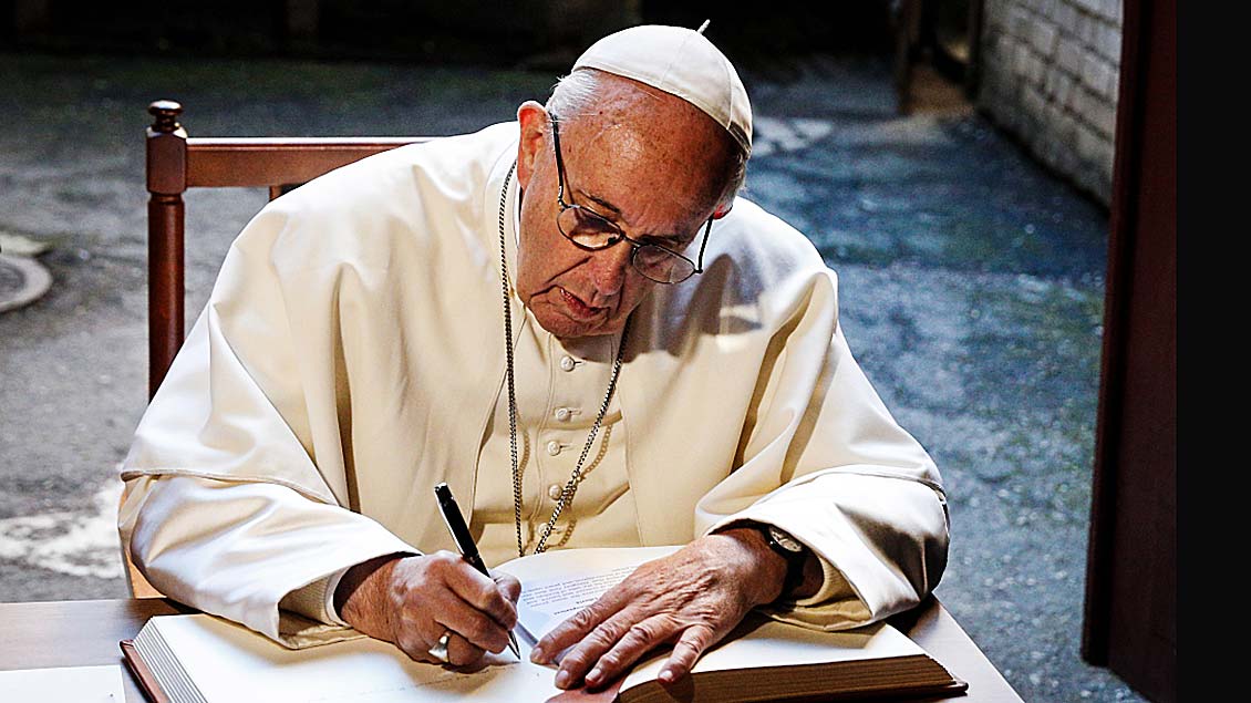 Papst Franziskus schreibend an einem Tisch Foto: Paul Haring (KNA)