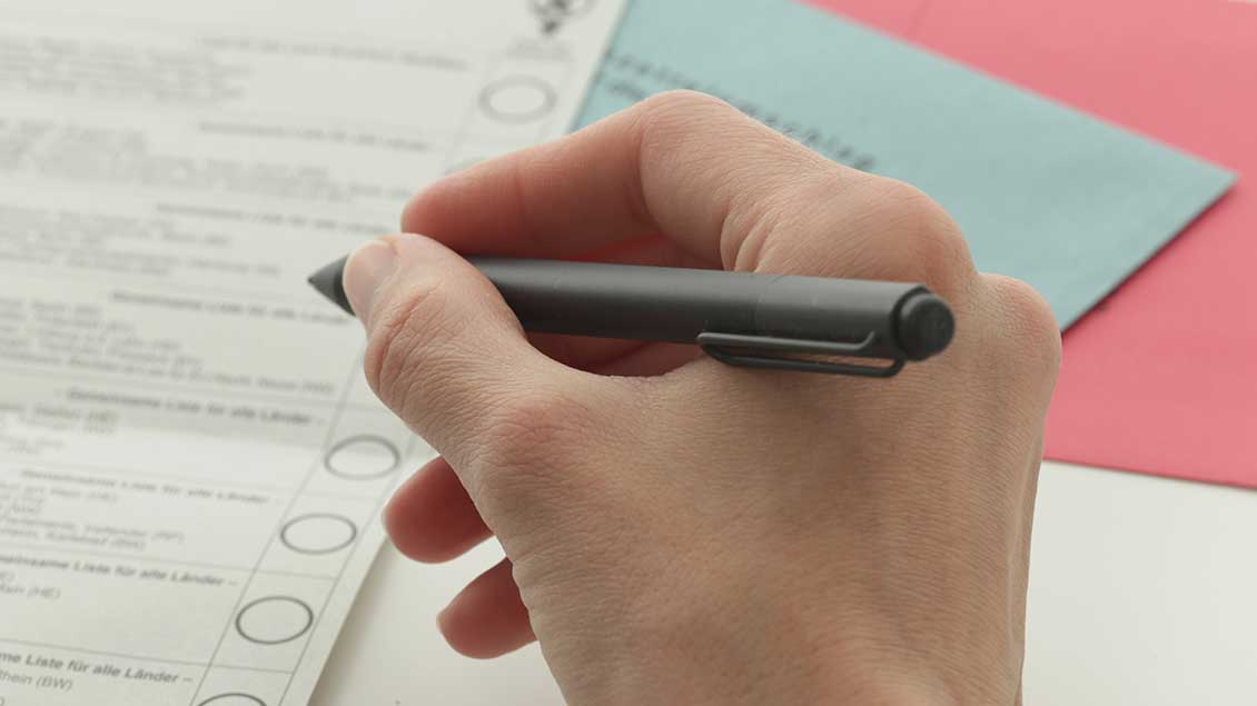 Hand mit Kugelschreiber vor Stimmzetteln