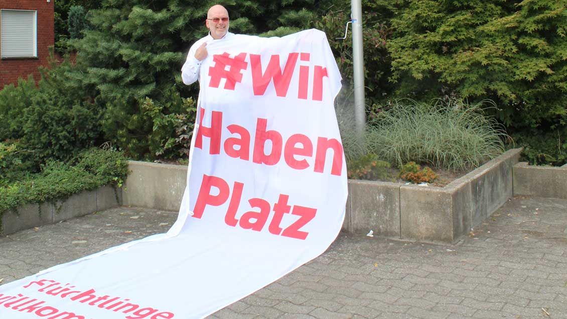 Pfarrer Happe mit dem Banner #wir haben Platz