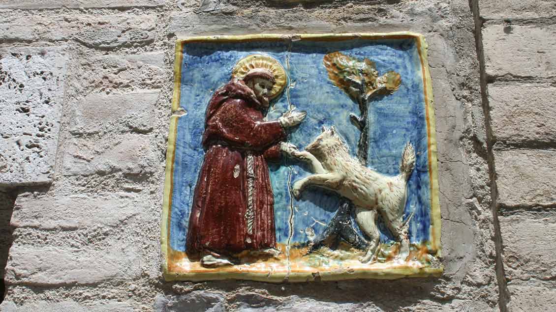 Eine Kachel an der Mauer eines Wohnhauses in Assisi zeigt die tiefe Verbundenheit des heiligen Franziskus mit der Schöpfung: der Legende zähmte er einen gefürchteten Wolf. | Foto: Markus Nolte