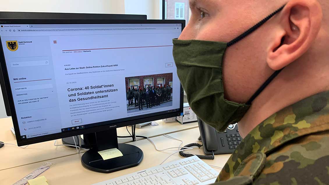 Soldat mit Mund-Nasen-Bedeckung vor einem Computer