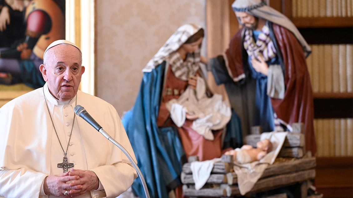Papst Franziskus steht in der päpstlichen Bibilothek vor einer Krippe und spricht an einem Mikrofon.
