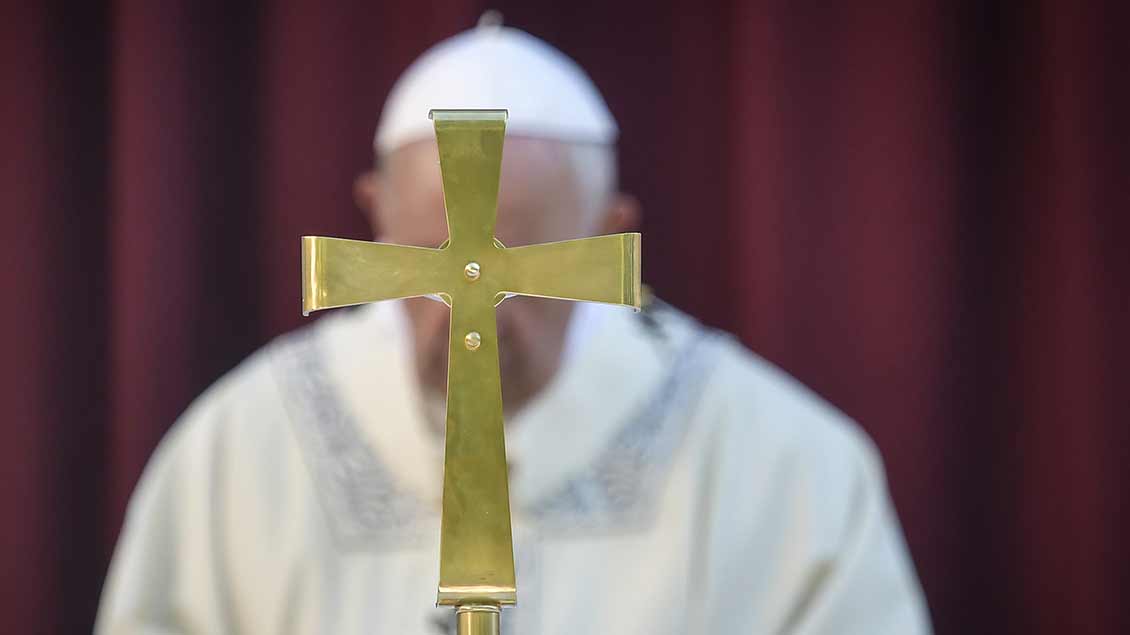 Papst Franziskus hinter einem Kreuz.