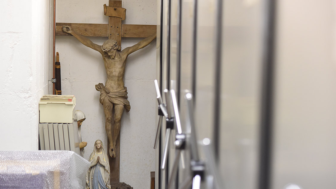 In dem Magazin eines Museums stehen Kreuze und Heiligenfiguren zwischen den Archivschränken.