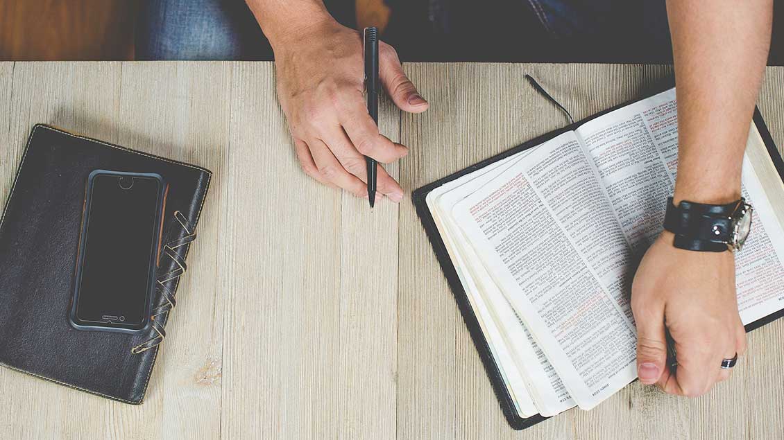 Bibel auf dem Tisch, daneben Handy und Notuzblock
