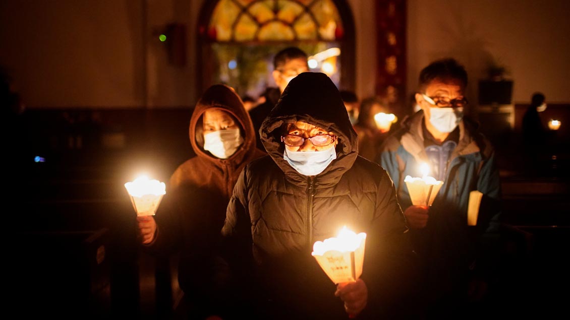 Glaäubige mit Kerzen in dunkler Kirche in Shanghai.
