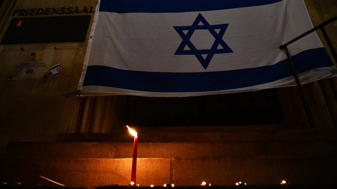 Vor einer Landesflagge Israels brennt eine Kerze.