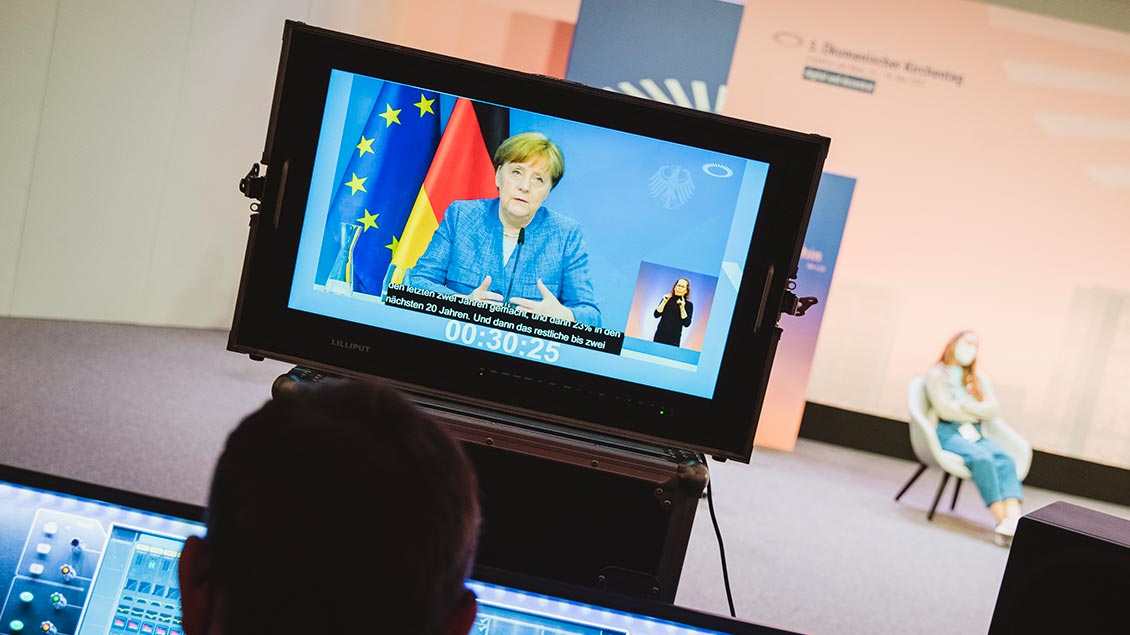 Angela Merkel auf einem Bildschirm beim Ökumenischen Kirchentag.