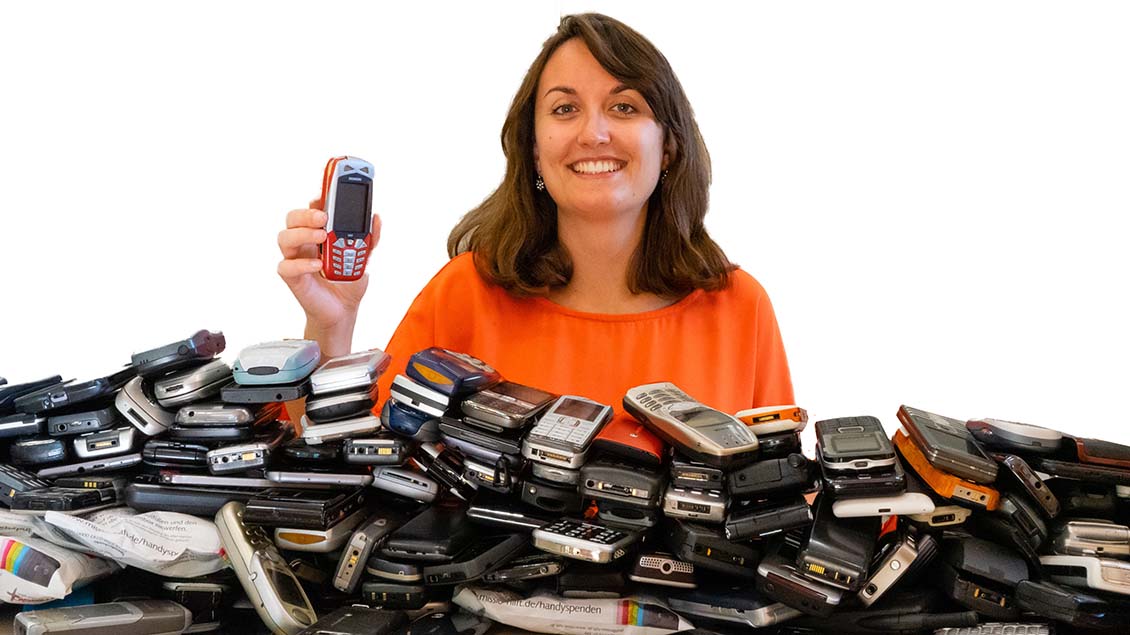 Eine Frau steht vor einem Berg von alten Handys.