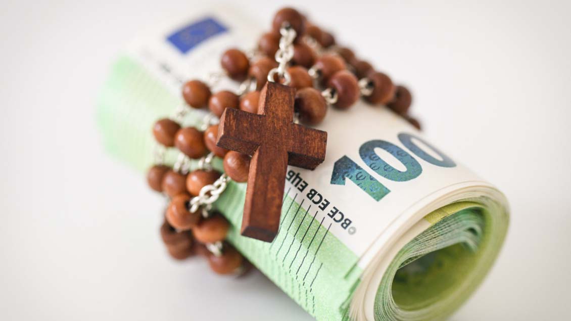 Ein Rosenkranz ist um ein Bündel von Geldscheinen gewickelt. Foto: KNA