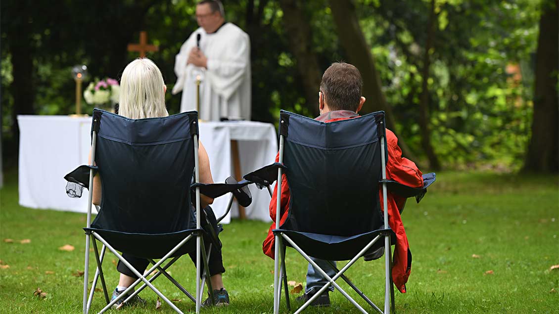 Zwei Gottesdienstteilnehmer sitzen in Klappstühlen auf der Wiese. Foto: Michael Bönte