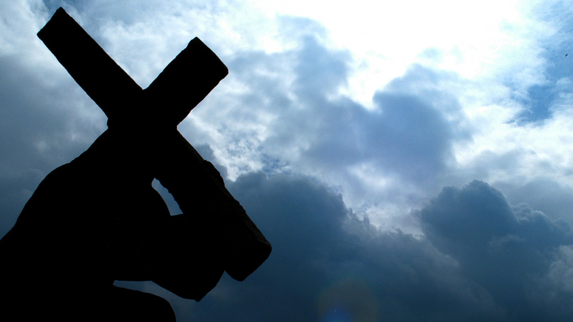 Die dunkle Silouette eines Kreuzes vor bedrohlichen Wolken.
