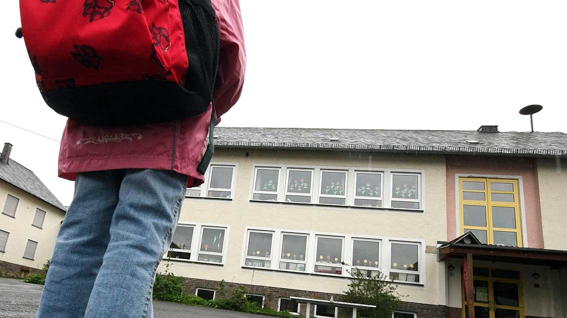 Kind mit Schulranzen vor einer Schule