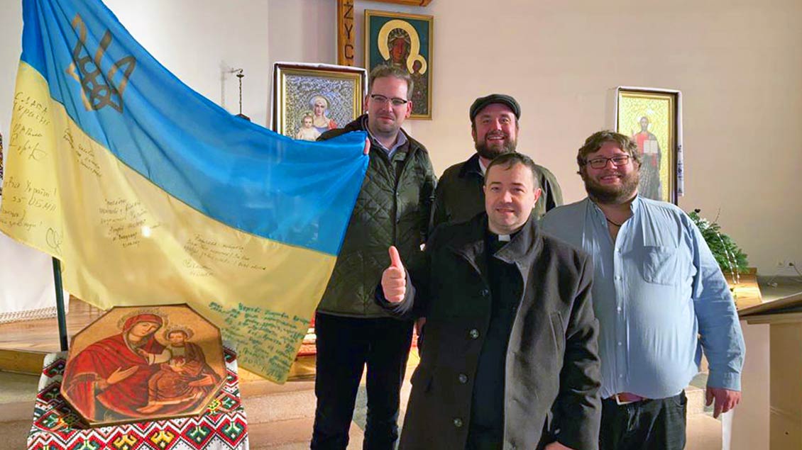 Der Pfarrer der ukrainischen Gemeinde in Warschau (vorne) gab Marco Schomacher, Max Dreckmann und Max Eickmann (von links) einen Einblick in das Leben der Gemeinde und zeigte ihnen eine ukrainische Flagge