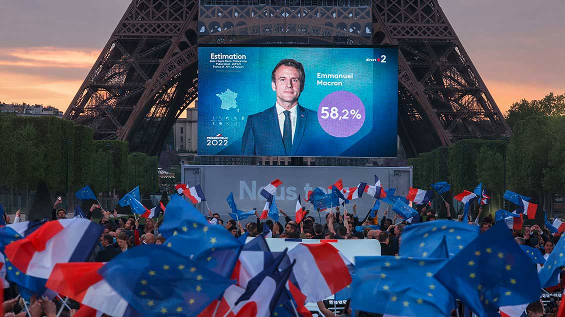 Menschen vor dem Eiffelturm in Paris mit Bild von Emmanuel Macron