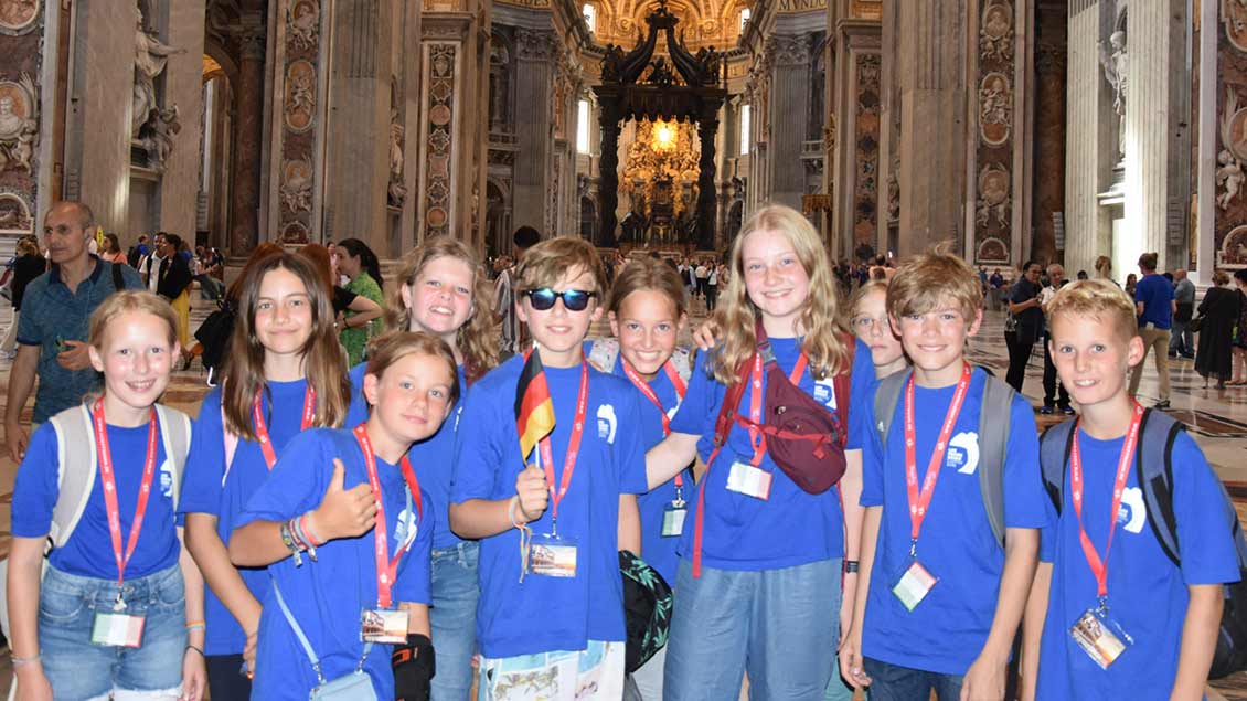 Kinder in blauen Shirts stehen im Petersdom und lächeln in die Kamera. Foto: Markus Stindt