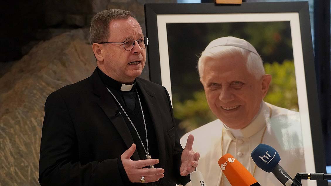 Bischof Georg Bätzing vor einem Porträtbild von Benedikt XVI.