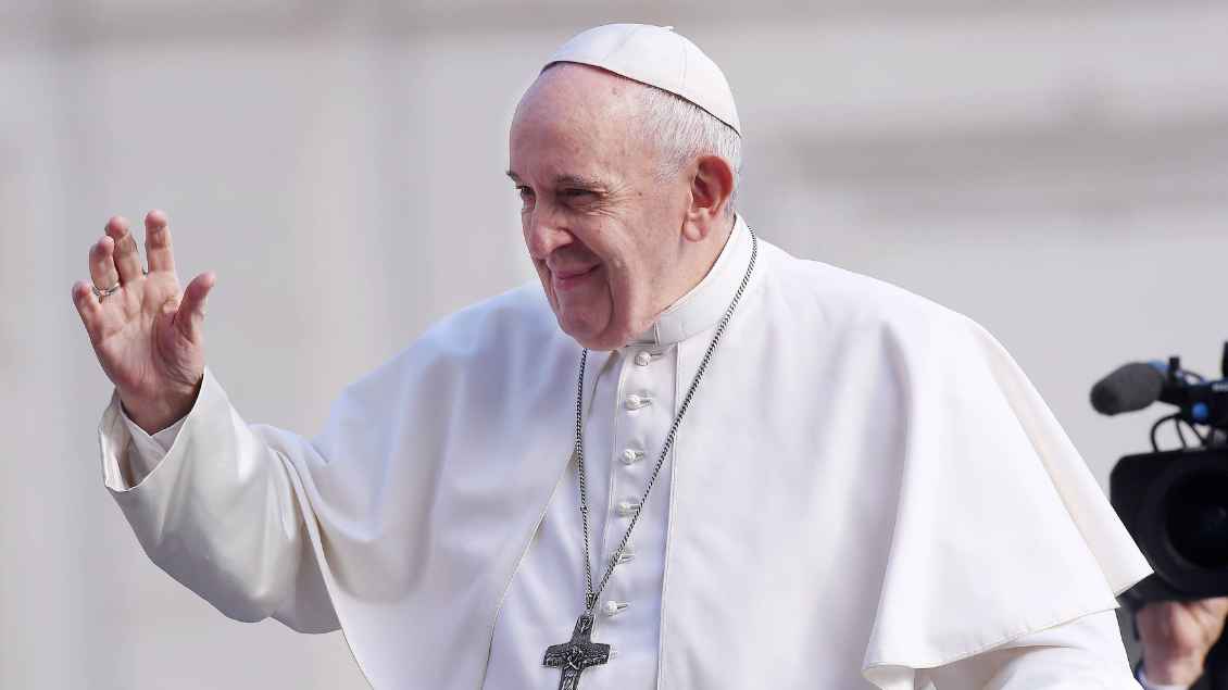 Papst Franziskus winkt mit der rechten Hand. Im Hintergrund ist eine Fernsehkamera zu sehen.