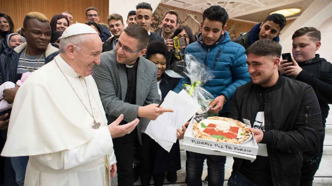 Papst Franziskus wird eine Pizza gereicht.
