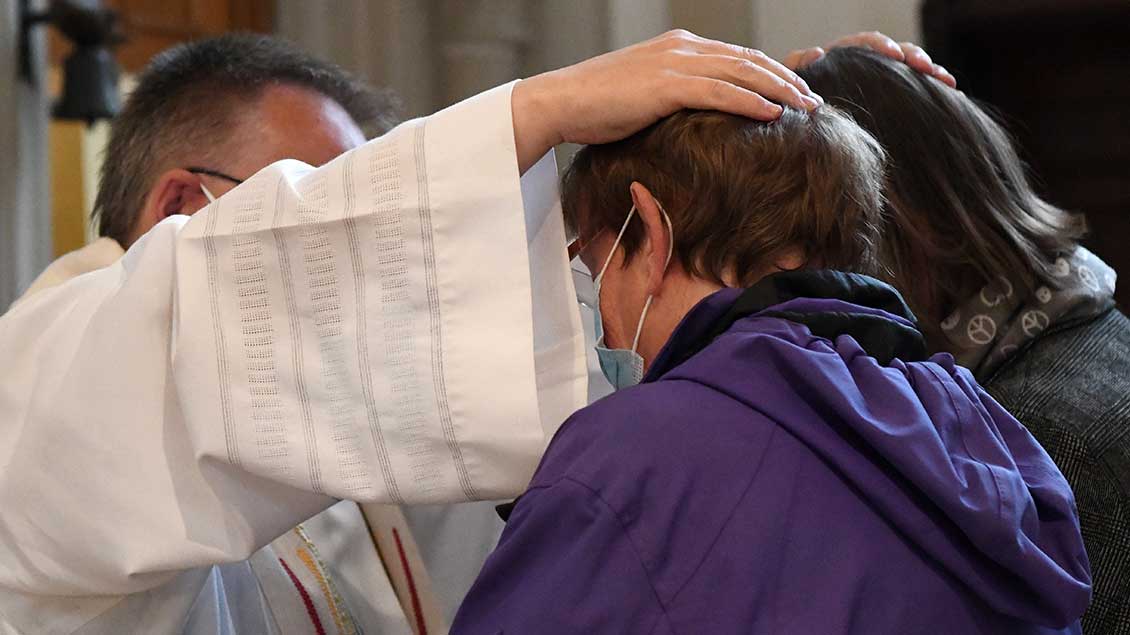 Ein Pfarrer in weißem Gewand hält jeweils eine Hand auf zwei Köpfe. Foto: Michael Bönte