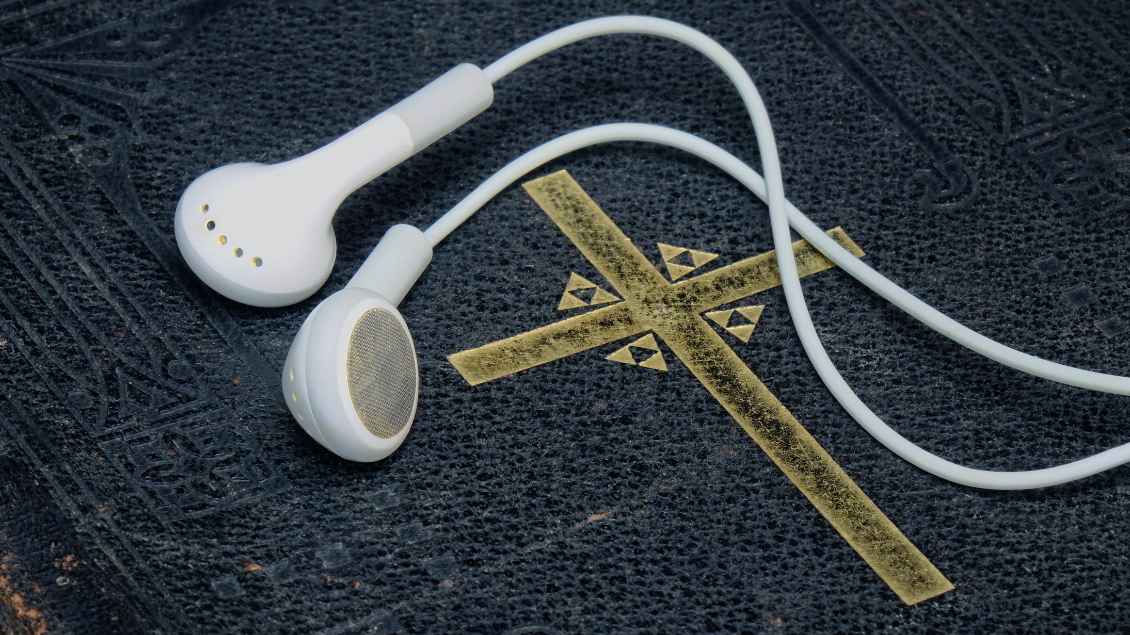 Kopfhörer liegen auf einer schwarzen Bibel mit dem Aufdruck eines goldenen Kreuzes.