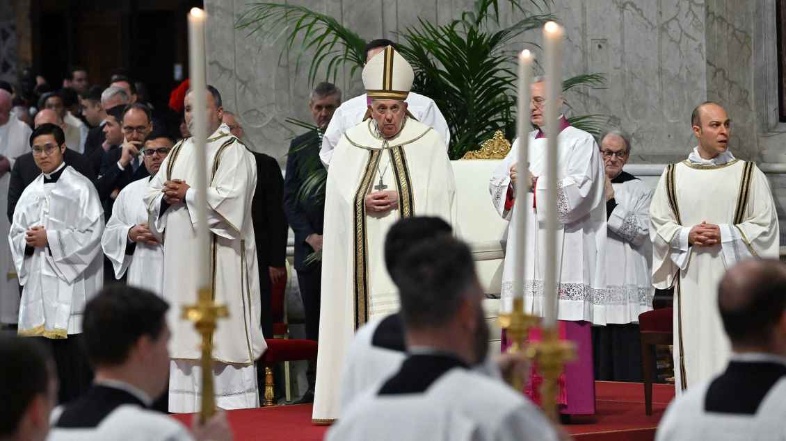 Papst Franiskus steht vor seinem Stuhl umringt von Messdienern un Geistlichen.