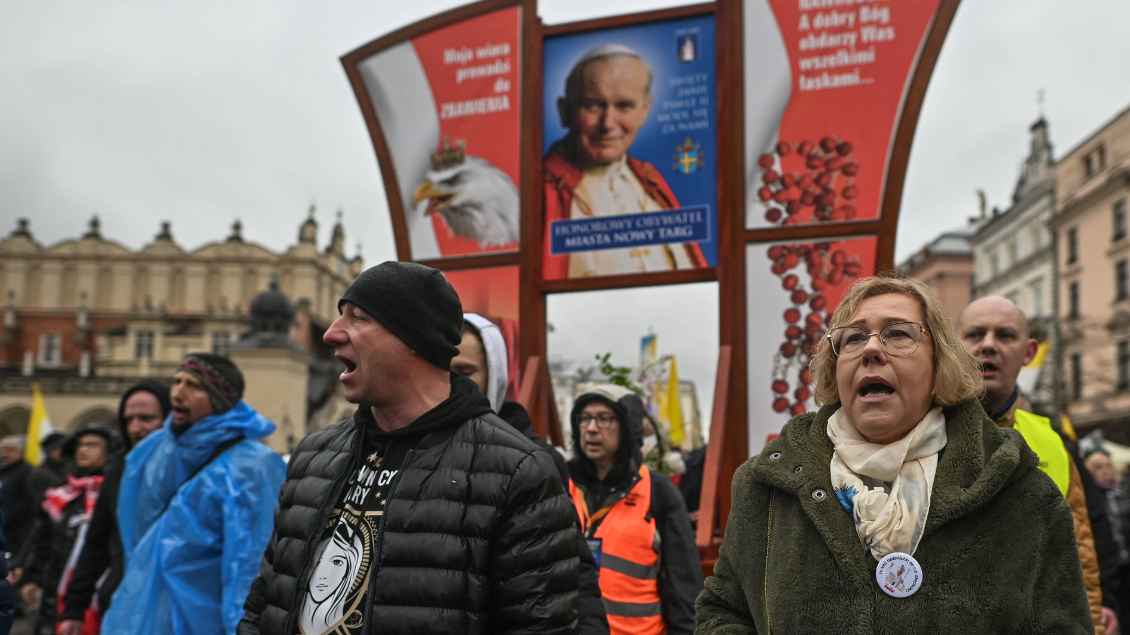 Menschen demonstrieren im Regen. Sie halten ein Bild von Papst Johannes Paul II. in die Höhe.
