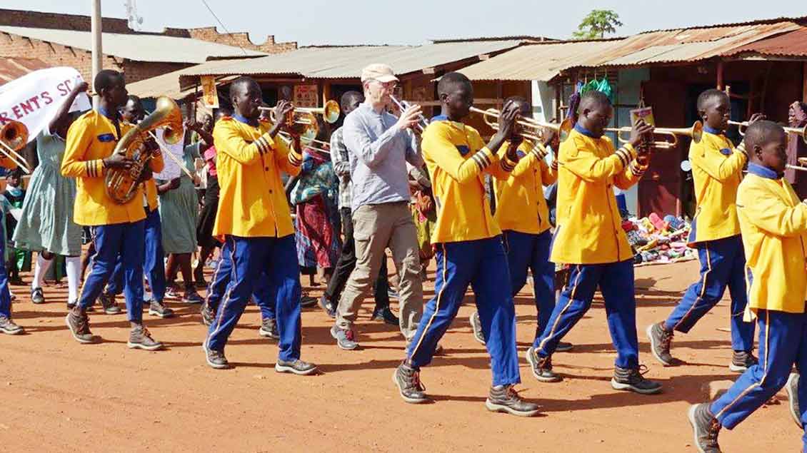 Mit Trompeten und Posaunen marschieren die Mitglieder der Brass-Band und Thomas Stählker durch Obiya Palaro in Uganda.
