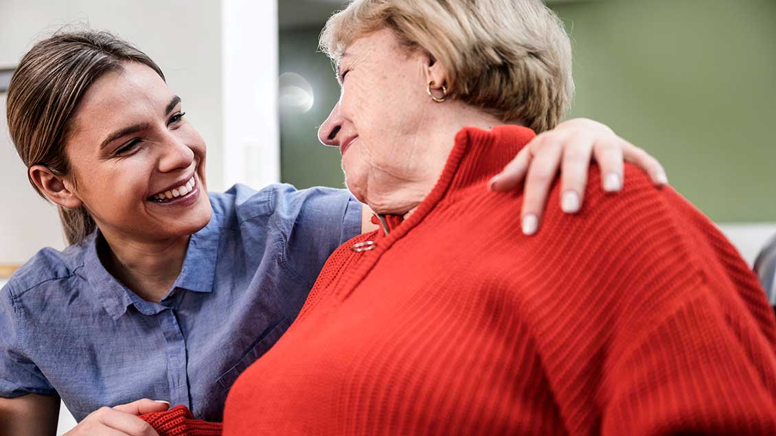 Eine Pflegekraft lächelt eine Seniorin an