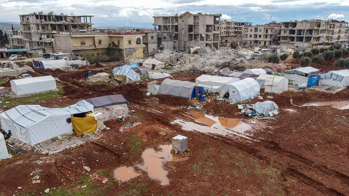 Zeltstadt mit großen Pfützen vor erdbebenzerstörten Häusern in Syrien