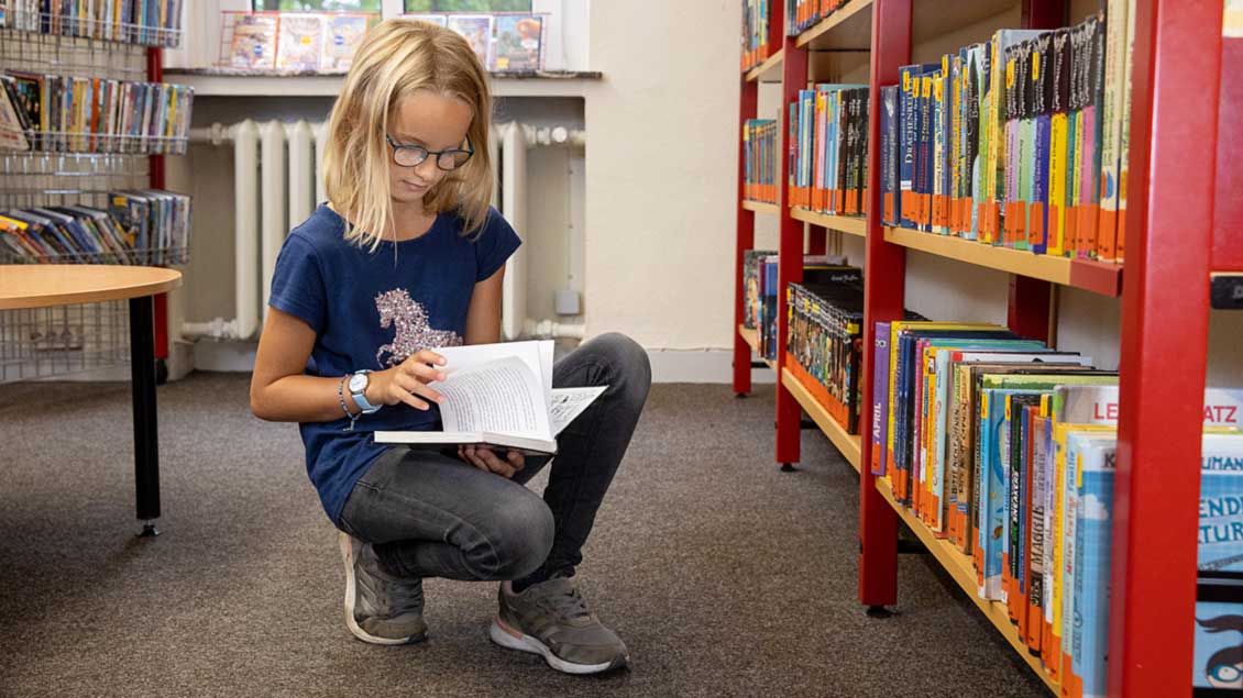 Kind kniet vor einem Regal in einer Bücherei