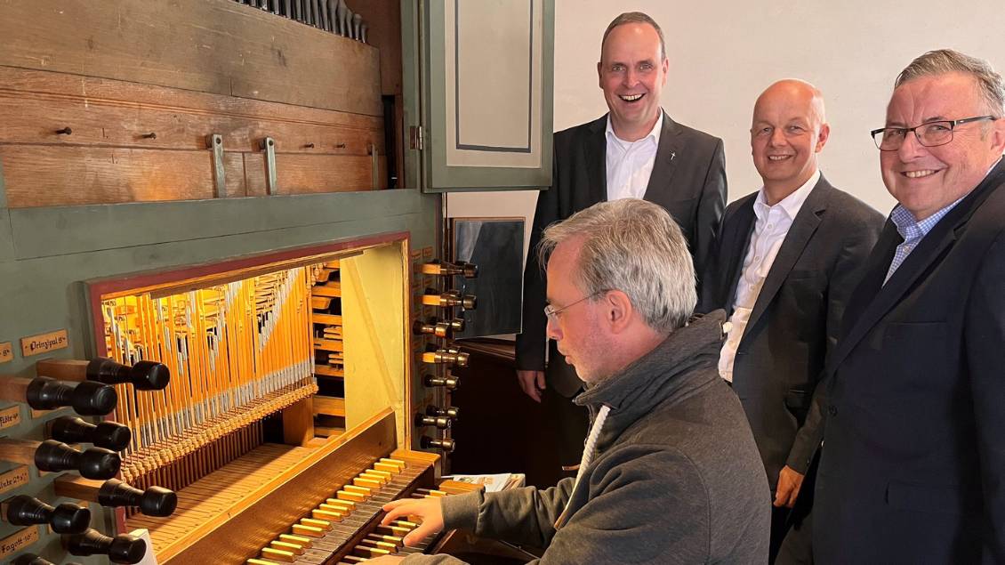 Mehrer Männer stehen lächelnd vor einer alten Orgel. Eine Person sitzt an dem Instrument und bedinet die Tasten. Foto: Peter Berger