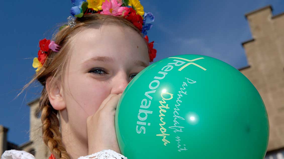 Ein Mädchen bläst einen Luftballon mit dem Logo von Renovabis auf.