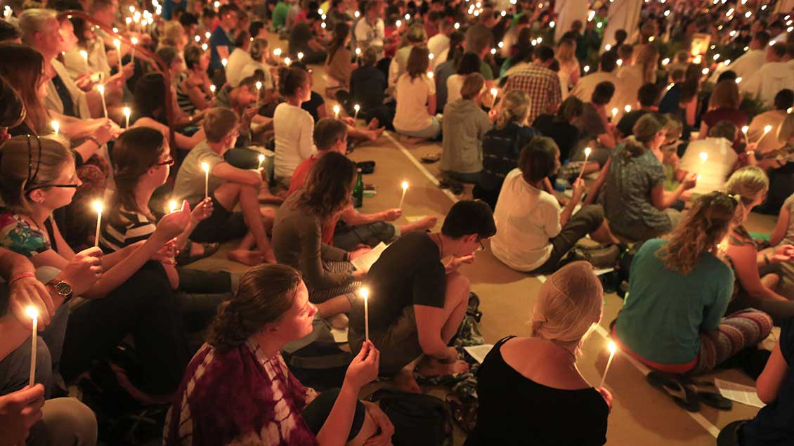 Menschen knien mit Kerzen während eines Taizé-Gebets