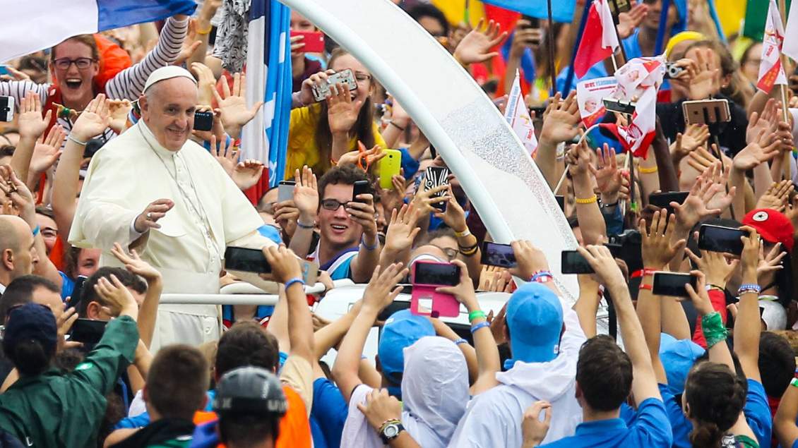 Papst Franziskus winkt aus seinem Papamobil jungen Menschen zu.