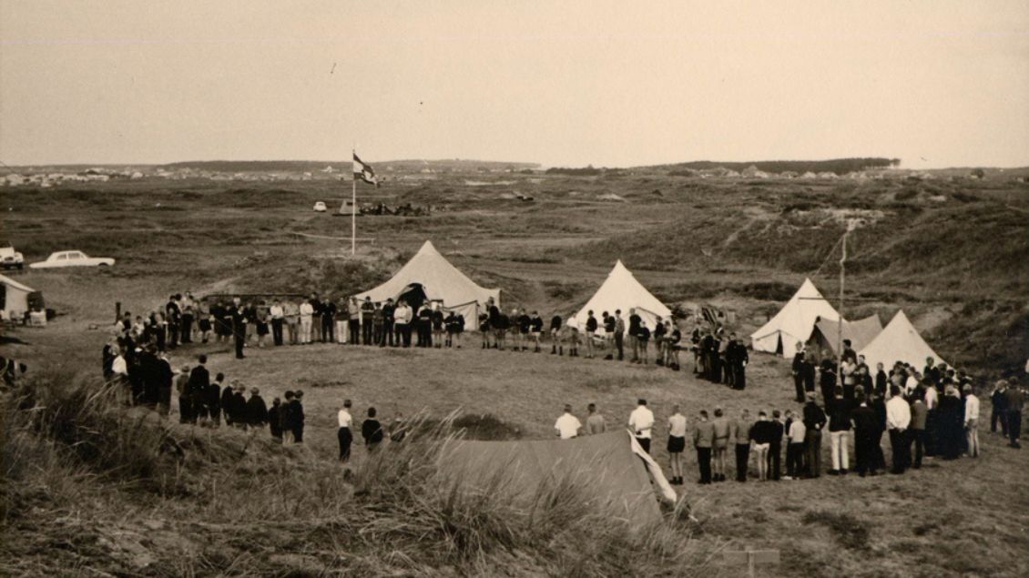 Ein Schwarz-/Weißbild. Viele Menschen stehen in einem Kreis in den Dünen. Es sind Zelte zu sehen. Foto: Heinz Emings „Schatzkiste“ (Heimatverein Borken)