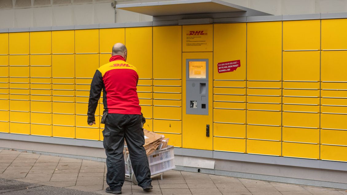 Ein Postbote steht vor einer gelben Paketstation. Symbolbild: Dirk Sattler (imago)