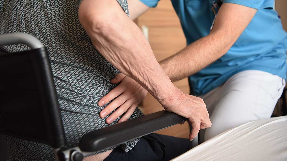 Pfleger hilft Patien in den Rollstuhl