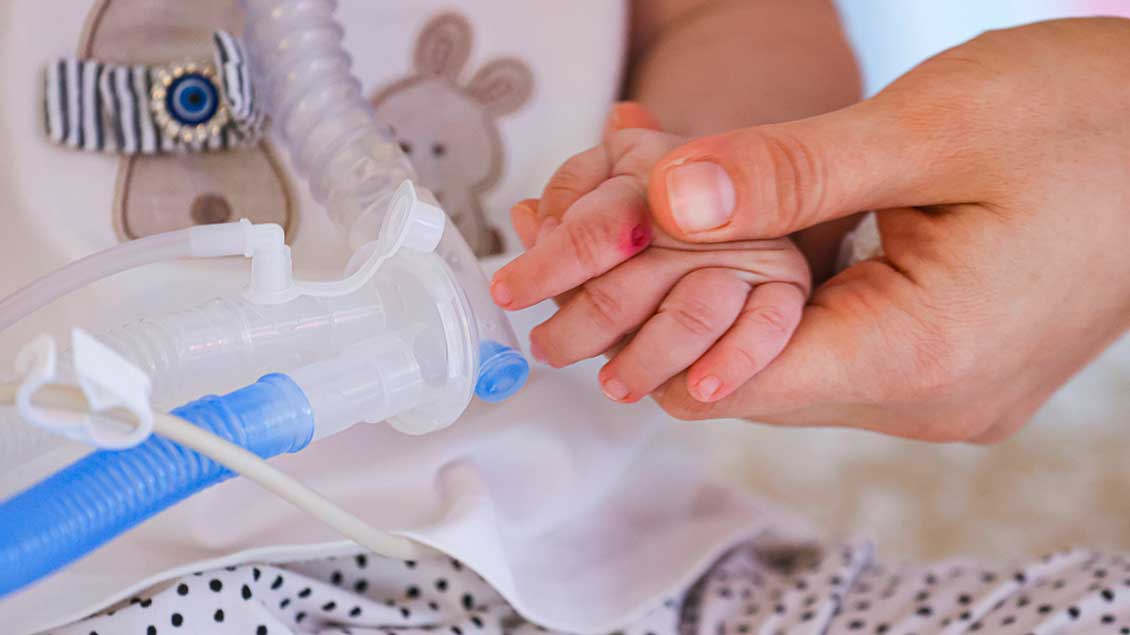Hand eines Erwachsenen hält Hand eines Kleinkindes im Krankenhausbett Symbolfoto: Imago