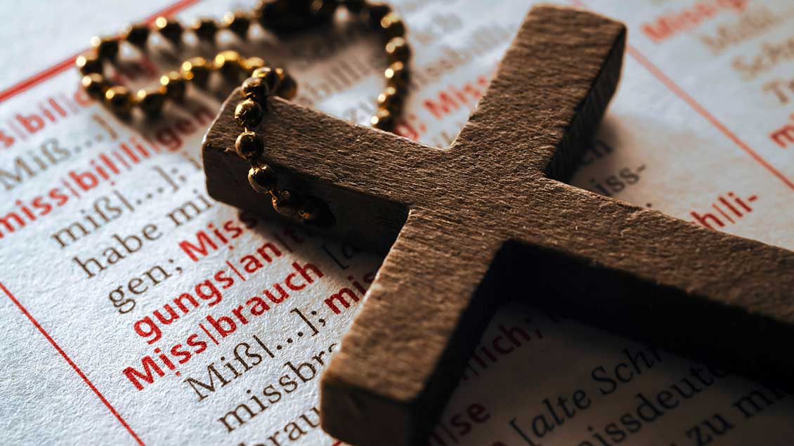 Ein Kreuz liegt auf einem Wörterbuch mit dem Eintrag "Missbrauch"