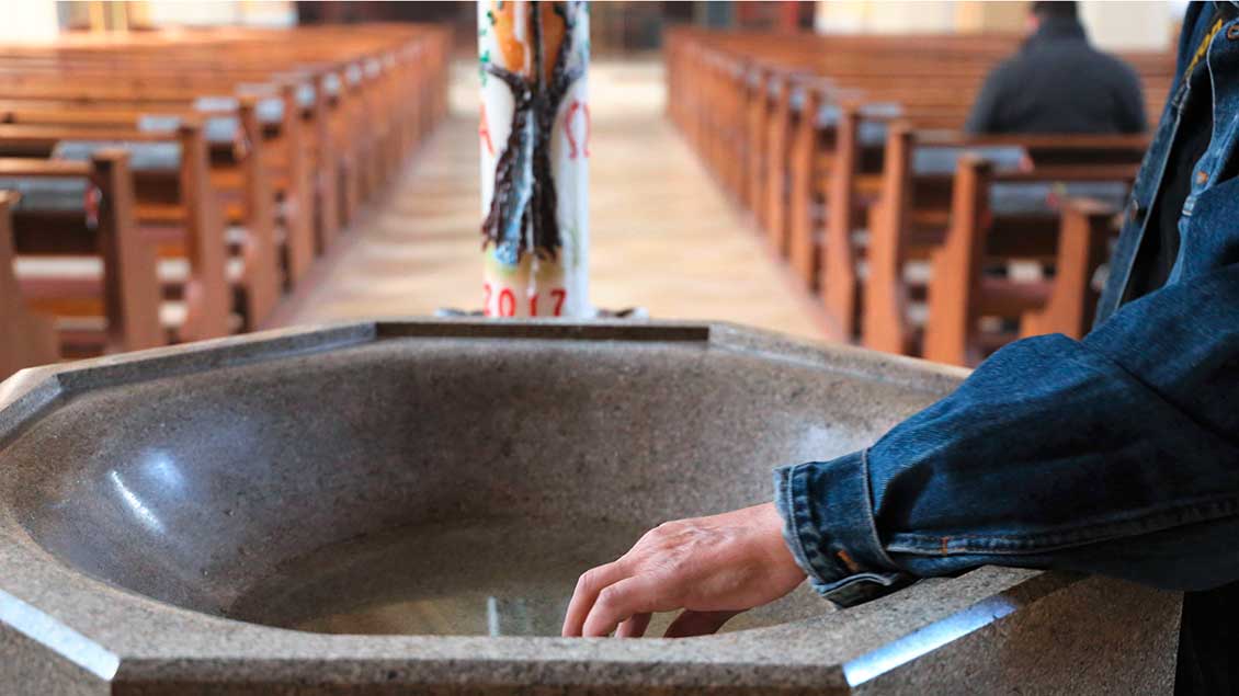 Ein Mensch taucht seine Hand ins Weihwasserbecken einer Kirche