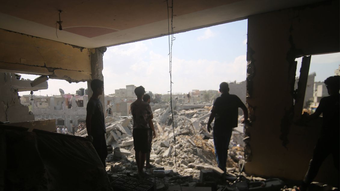 Personen schauen aus einem Gebäude auf Ruinen und Trümmer. 