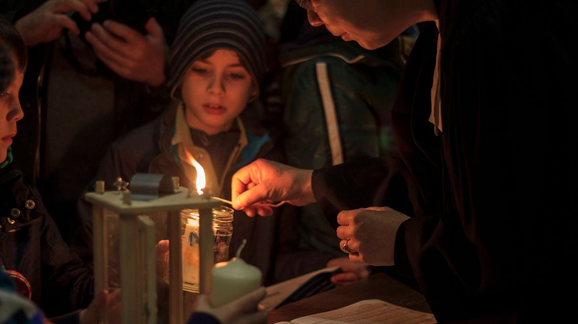 Kinder stehen mit Kerzen in der Hand um eine Laterne herum.