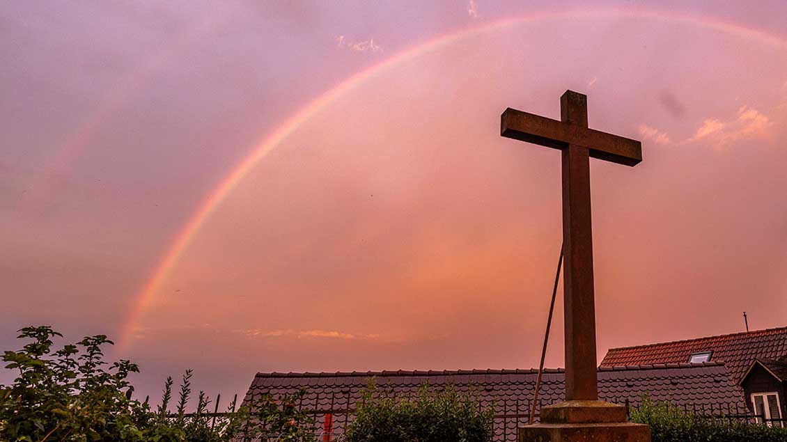 Kreuz unter einem Regenbogen auf rötlichem Himmel