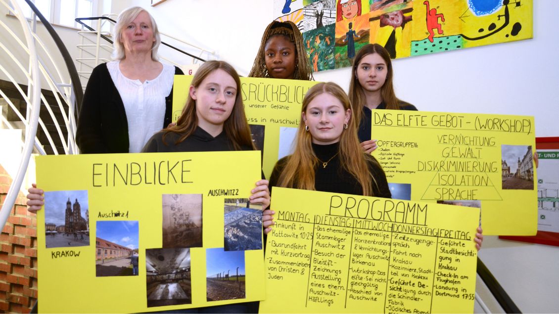 Junge Frauen und eine Lehrerin stehen auf einer Treppen und halten gelbe Plakate vor sich.