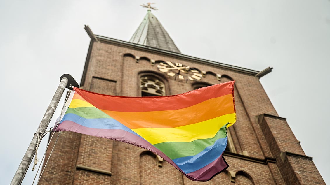 Regenbogenfahne vor einem Kirchturm