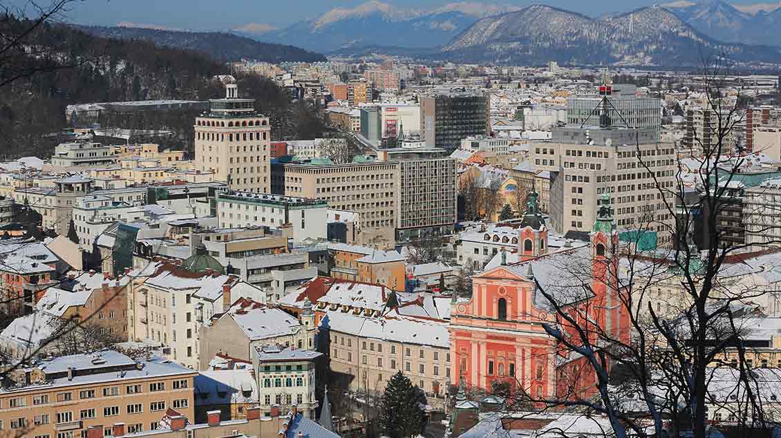 Blick über Ljubljana im Winter mit Franziskanerkirche und Bergen im Hintergrund